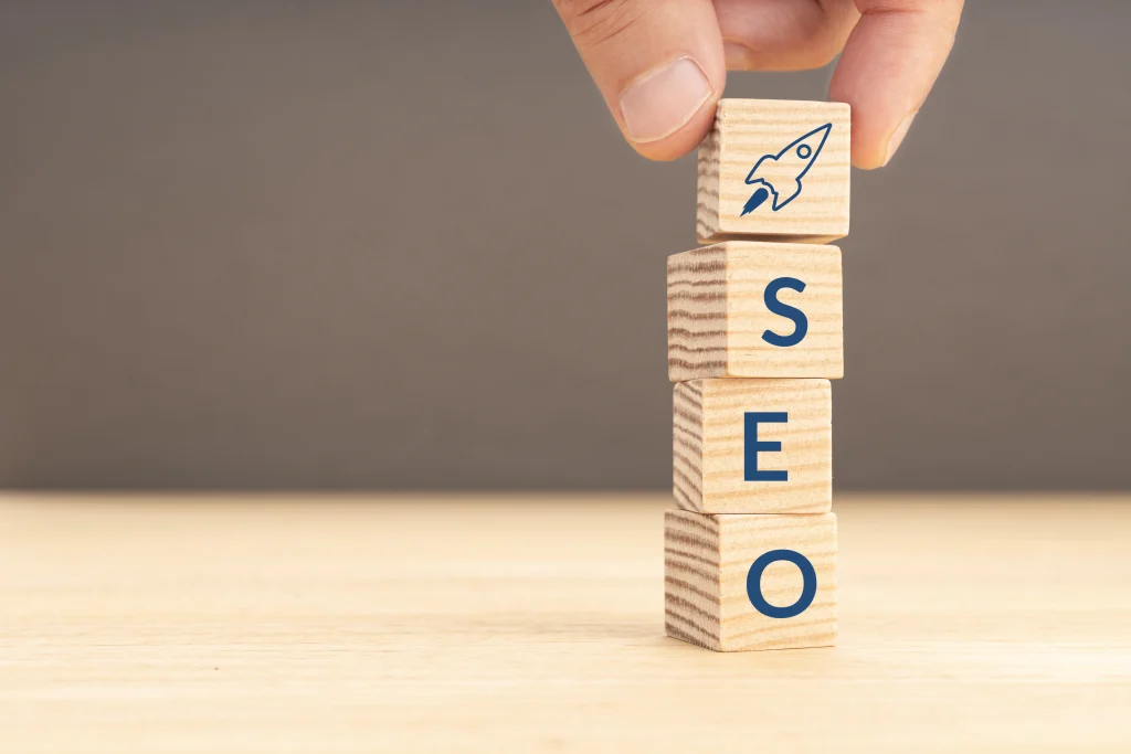 A hand arranges wooden blocks spelling “SEO Company NYC” with a rocket icon on a light wood surface.