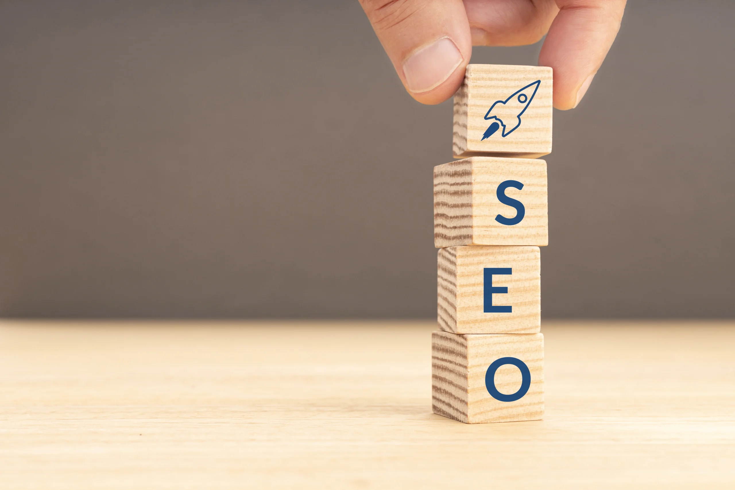 A hand arranges wooden blocks spelling “SEO Company NYC” with a rocket icon on a light wood surface.